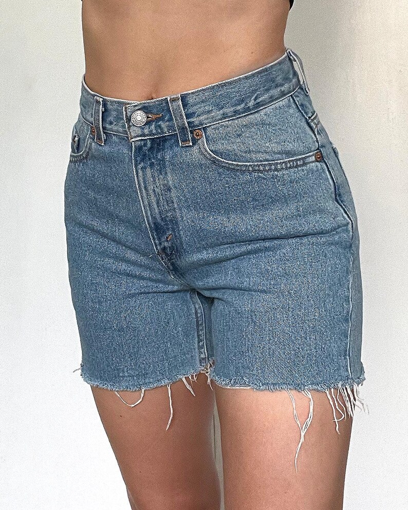 K&ouml;nnte beinhalten: Hellblaue Jeans-Shorts mit ausgefranstem Saum. Die Shorts haben eine hohe Taille und f&uuml;nf Taschen.