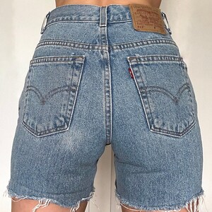 K&ouml;nnte beinhalten: Hellblaue Jeans-Shorts mit ausgefranstem Saum. Die Shorts haben einen hohen Bund und ein Levi's-Etikett auf der rechten Ges&auml;&szlig;tasche. Das Etikett lautet "Levi's&reg; Original Quality Clothing" und "512&trade;".