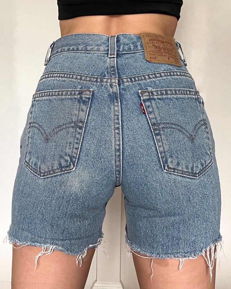 K&ouml;nnte beinhalten: Hellblaue Jeans-Shorts mit ausgefranstem Saum. Die Shorts haben einen hohen Bund und ein Levi's-Etikett auf der rechten Ges&auml;&szlig;tasche. Das Etikett lautet "Levi's&reg; Original Quality Clothing" und "512&trade;".