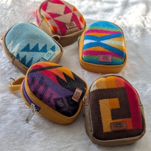 May include: Five small, colorful, patterned pouches with zipper closures. The pouches are made of a soft, woven fabric and have a brown leather trim. The pouches are all different colors and patterns, including blue, green, red, yellow, and brown.