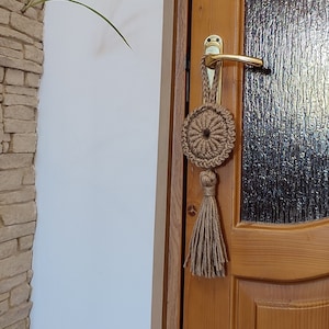 Peut inclure: Une porte en bois avec un panneau en verre et une poignée de porte dorée. Un pompon en macramé pend à la poignée.