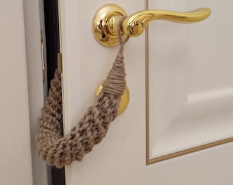 May include: A close-up of a door with a gold door handle and a brown rope doorstop. The doorstop is made of a woven material and is attached to the door handle.