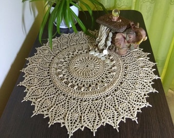 May include: A beige crocheted doily with a circular design and intricate details. The doily is laid on a dark brown wooden table.