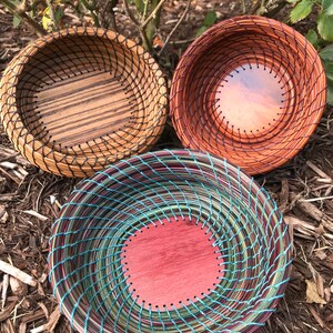 Puede incluir: Tres cestas tejidas con diferentes tejidos de colores y patrones. Las cestas est&aacute;n hechas de materiales naturales y tienen una forma redonda. Las cestas est&aacute;n sentadas en un lecho de mantillo marr&oacute;n.