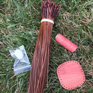 Puede incluir: Un haz de juncos de tejido de fibra natural marr&oacute;n, una bobina de hilo rosa, una peque&ntilde;a bola blanca en una bolsa de pl&aacute;stico transparente y un telar redondo de madera con agujeros alrededor del borde.