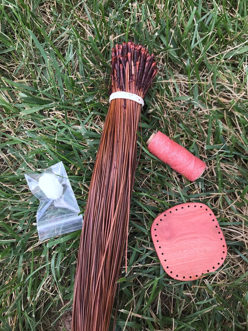 Puede incluir: Un haz de juncos de tejido de fibra natural marr&oacute;n, una bobina de hilo rosa, una peque&ntilde;a bola blanca en una bolsa de pl&aacute;stico transparente y un telar redondo de madera con agujeros alrededor del borde.