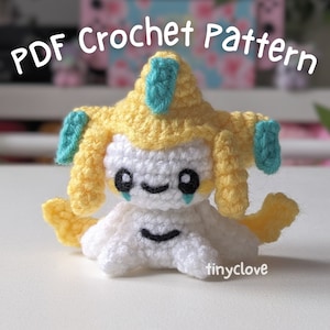 Peut inclure: Jouet amigurumi en crochet représentant un personnage de Pokemon avec des cheveux jaunes, un corps blanc et des accents bleus. Le jouet est assis sur une surface blanche. Le texte "PDF Crochet Pattern" est visible en haut de l'image.