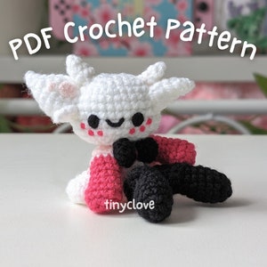 May include: White crocheted amigurumi toy with pink cheeks, black bow tie, and red and black crocheted clothing. The toy is sitting on a white surface. The text "PDF Crochet Pattern" is at the top of the image.
