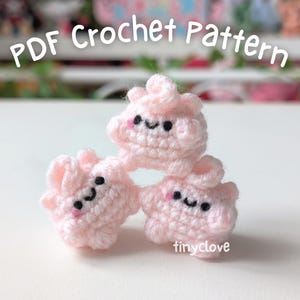 May include: Three pink crocheted plushies with smiling faces. The plushies are stacked on top of each other. The plushies are made with a soft, fluffy yarn.