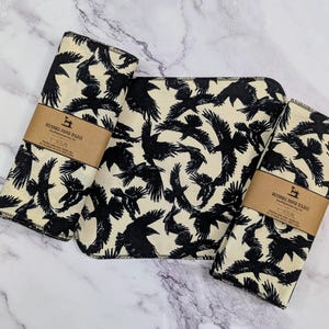 May include: Three reusable paper towels with a black and white crow print. The towels are folded and have a brown label that reads "Reusable Paper Towels".