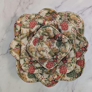 Pode incluir: Um conjunto de bases de tecido com tema natalino em vários tamanhos. As bases apresentam um padrão festivo com luvas vermelhas, ursinhos de pelúcia e detalhes verdes em um fundo creme. As bases são dispostas em forma de flor.