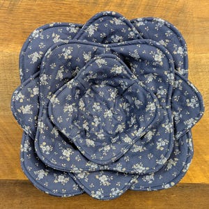 May include: A set of three nested, square-shaped fabric bowl cozies featuring a dark blue background with a repeating white floral pattern. Each cozy has rounded corners, quilted stitching, and a soft, padded construction for holding bowls.