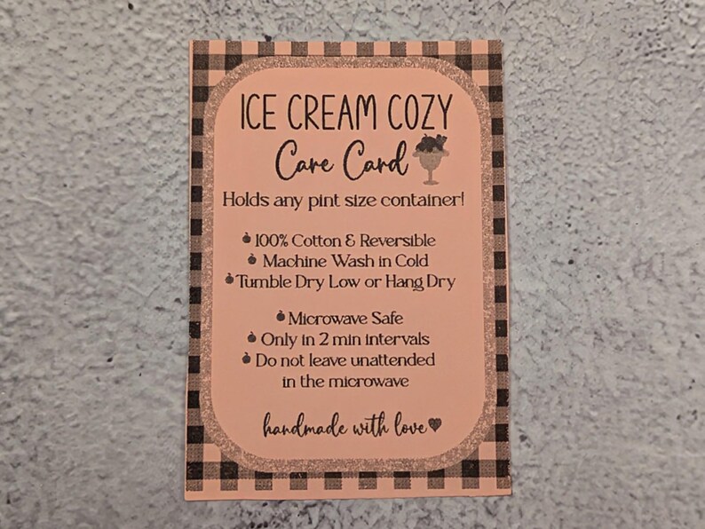 May include: A peach-colored care card for an ice cream cozy, with black text and a gingham border. The card details care instructions, including being microwave safe and made of 100% cotton. The text reads "handmade with love."