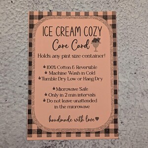 May include: A peach-colored care card for an ice cream cozy, with black text and a gingham border. The card details care instructions, including being microwave safe and made of 100% cotton. The text "handmade with love" is at the bottom.