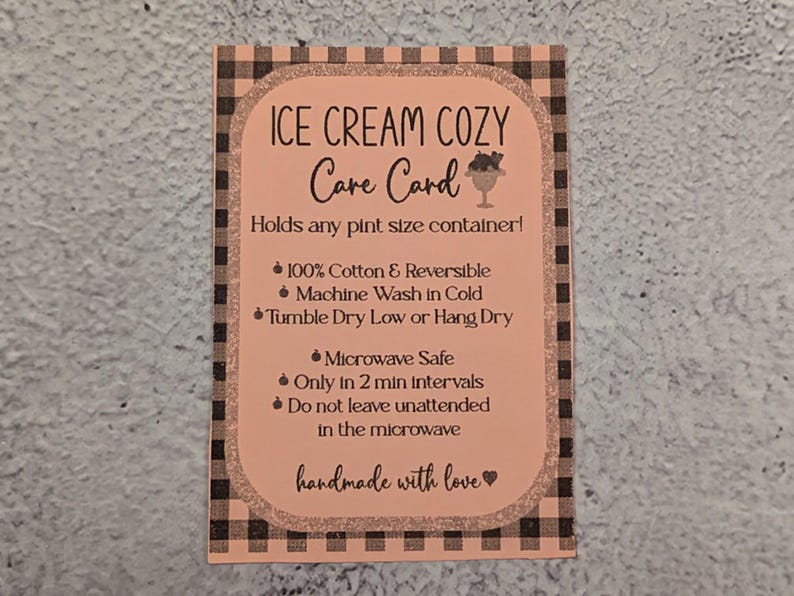 May include: A peach-colored care card for an ice cream cozy, with black text and a gingham border. The card details care instructions, including being microwave safe and made of 100% cotton. The text "handmade with love" is at the bottom.