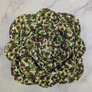May include: A set of quilted, floral-shaped pot holders and bowl cozies. The fabric features a pattern of green holly leaves, brown pinecones, and red berries on a white background. The set includes various sizes.