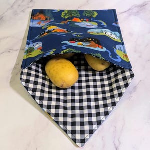 Può includere: Una borsa per sandwich riutilizzabile blu navy con una stampa di scena di campeggio, aperta per rivelare due patate. L'interno è a scacchi bianchi e neri. La borsa è progettata per contenere alimenti.