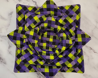 May include: Set of four purple and green plaid fabric bowl cozies. The cozies are folded into a star shape and are stacked on top of each other.