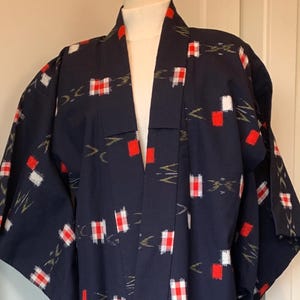 May include: Navy blue kimono-style robe with a repeating pattern of red and white squares and gold accents. The robe is open in the front and has wide sleeves. A traditional garment.