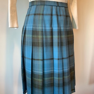 May include: A knee-length pleated skirt featuring a blue plaid design with green and brown accents. The skirt has a tailored waistband and is made from a medium-weight fabric. The design is reminiscent of classic tartan patterns.