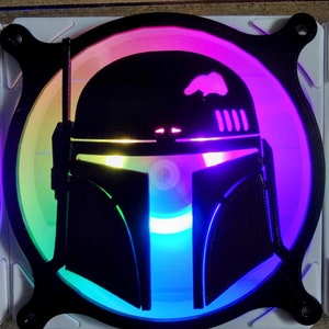 May include: A black plastic fan with a colorful LED light display featuring a silhouette of a Star Wars character's helmet. The helmet is a dark gray color and has a visor. The fan is illuminated with a rainbow of colors, including red, orange, yellow, green, blue, indigo, and violet.