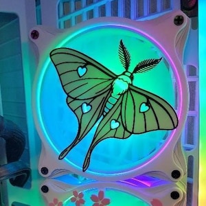 Puede incluir: Dos ventiladores de ordenador con marcos blancos e iluminación LED colorida. El ventilador superior presenta un diseño de polilla verde con detalles de corazón. El ventilador inferior tiene un diseño de flor de cerezo rosa. Los ventiladores están montados en una caja de ordenador.