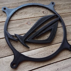 May include: A black plastic fan grill with a 3D printed ASUS ROG logo. The logo is a stylized eye with wings.