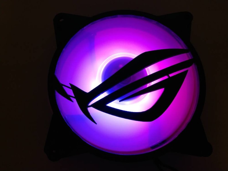 May include: A black computer fan with a purple and blue LED light. The fan has a black logo with the letters "ROG" in the center.
