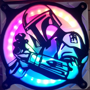 May include: A black and white silhouette of a Star Wars character, possibly a Mandalorian, is cut out and placed on a round, white fan with multi-colored LED lights. The fan is mounted on a white surface.