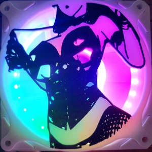 May include: A white computer fan with a black silhouette of a person wearing a corset and a hat. The fan has a multi-coloured LED light display.
