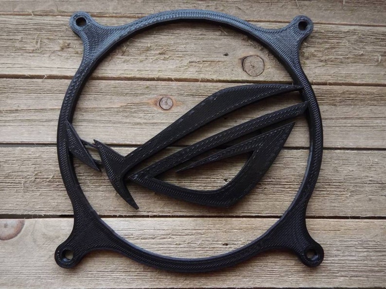 May include: A black plastic fan grill with the ASUS ROG logo printed on it. The grill is circular and has a textured surface.