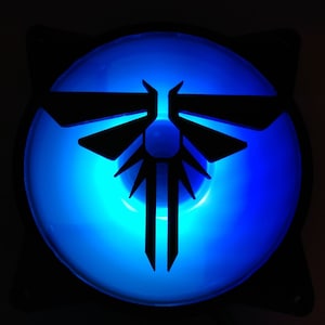 Może przedstawiać: Czarny wentylator komputerowy z niebieskim światłem i stylizowanym wzorem świetlika.