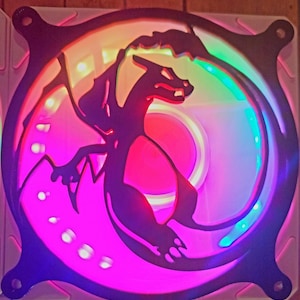 Puede incluir: Ventilador de ordenador con una silueta negra de dragón en el centro. El ventilador tiene un diseño circular con un marco negro y está iluminado con una vibrante gama de colores, incluyendo rosa, verde y azul.