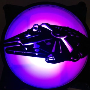 May include: A black plastic computer fan with a purple and white light behind it. The fan has a cutout of a spaceship in the center.