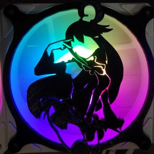 May include: A black silhouette of a person with long hair, holding a large object, is cut out of a round, clear plastic fan. The fan is lit with a rainbow of colours, including red, orange, yellow, green, blue, indigo, and violet.