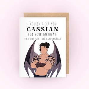 May include: A white card with a black and white illustration of a man with wings. The text on the card reads "I couldn't get you Cassian for your birthday. So I got you this card instead."