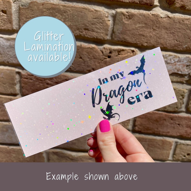 May include: A pink bookmark with iridescent glitter and the text "In my Dragon era" in black.