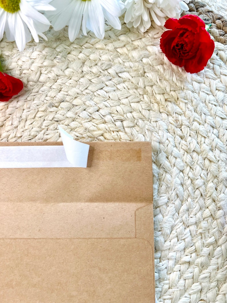 May include: A brown paper envelope with a white tape seal on a woven straw background.  White and red flowers are in the background.