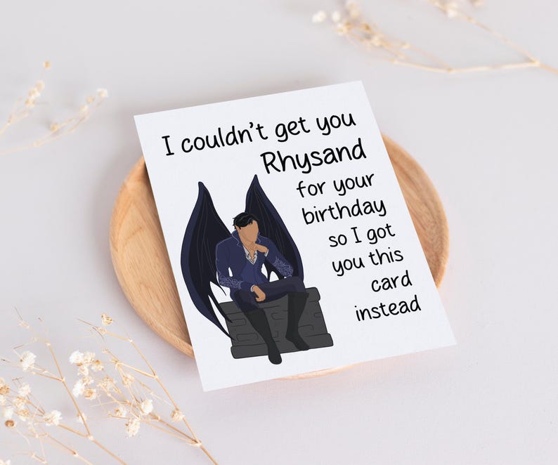 May include: A humorous birthday card featuring a black and white illustration of a character with wings sitting on a throne. The card reads "I couldn't get you Rhysand for your birthday so I got you this card instead."