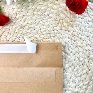 May include: A brown paper envelope with a white tape seal on a woven straw background.  White and red flowers are in the background.