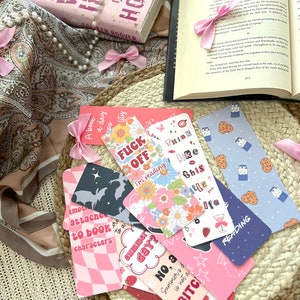 Puede incluir: Una colecci&oacute;n de marcadores coloridos con varios dise&ntilde;os y textos. Algunos de los marcadores presentan patrones de cuadros rosa y blanco, dise&ntilde;os florales y textos como "Think Like This" y "Summer Day?" Otros presentan una silueta negra de un murci&eacute;lago, un patr&oacute;n de cuadros rosa y blanco y textos como "Emotionally Attached to Book Characters" y "No, a Summer's Day is not a Bitch".