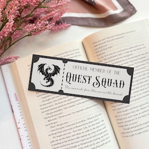 May include: A black and white bookmark with a dragon illustration and the text "Official Member of the Quest Squad The search for the seventh bread".