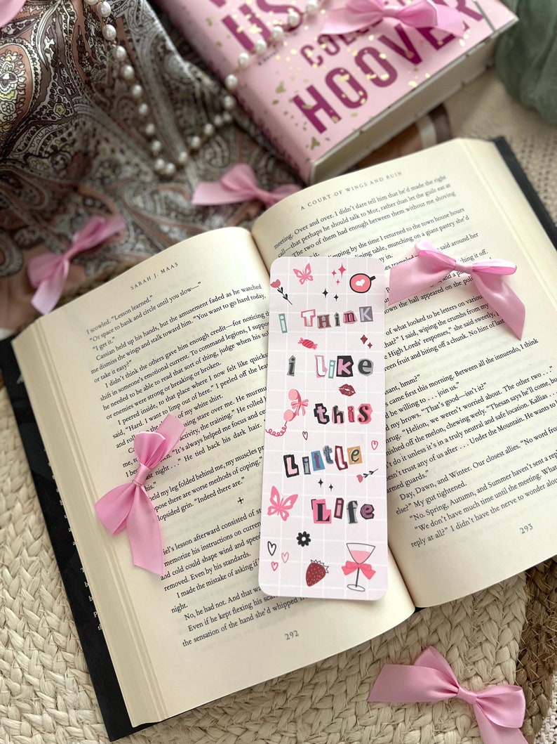 Puede incluir: Un marcap&aacute;ginas rosa y blanco con el texto "I think I like this little life" en una fuente retro colorida. El marcap&aacute;ginas presenta una mariposa rosa, una fresa y una copa de vino.