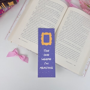 May include: Purple bookmark with a gold frame and the text "The One Where I'm Reading" on a blue background with white stars. The bookmark is a Friends themed bookmark.