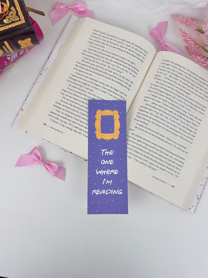 May include: Purple bookmark with a gold frame and the text "The One Where I'm Reading" on a blue background with white stars. The bookmark is a Friends themed bookmark.