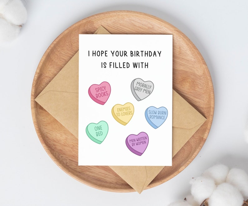May include: A birthday card with a humorous message and illustrations of candy hearts with various sayings, including "Spicy Books", "One Bed", "Enemies to Lovers", "Morally Grey Men", "Men Written by Women", and "Slow Burn Romance".