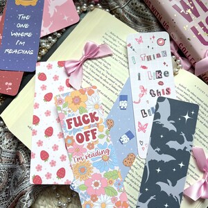 May include: A collection of colorful bookmarks with various designs. One bookmark features a floral pattern with the text "I'm reading". Another bookmark has a pink and white strawberry pattern. A third bookmark has a blue and white pattern with the text "Think I Like This". A fourth bookmark has a gray silhouette of bats with stars. A fifth bookmark has a blue and white pattern with the text "The One Where I'm Reading".