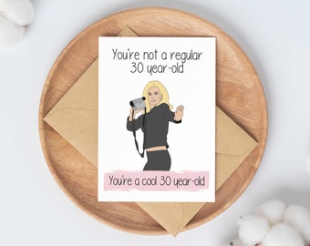 May include: A greeting card with a cartoon illustration of a woman holding a camcorder. The text on the card reads "You're not a regular 30 year-old. You're a cool 30 year-old."
