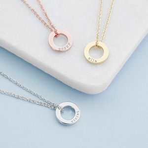 May include: Three necklaces with circular pendants, each featuring a delicate chain. One pendant is rose gold engraved with poppy, one is gold engraved with ella, and one is silver engraved with violet. The pendants are simple, flat rings.