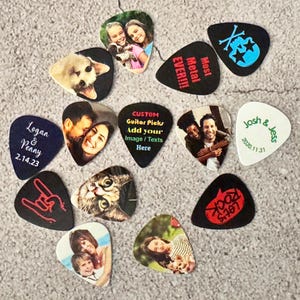 May include: A collection of custom guitar picks with various designs and photos. Some picks feature images of people, pets, and text like "Logan & Penny 2.14.23", "Most Metal Ever!!!", and "Let's Rock".